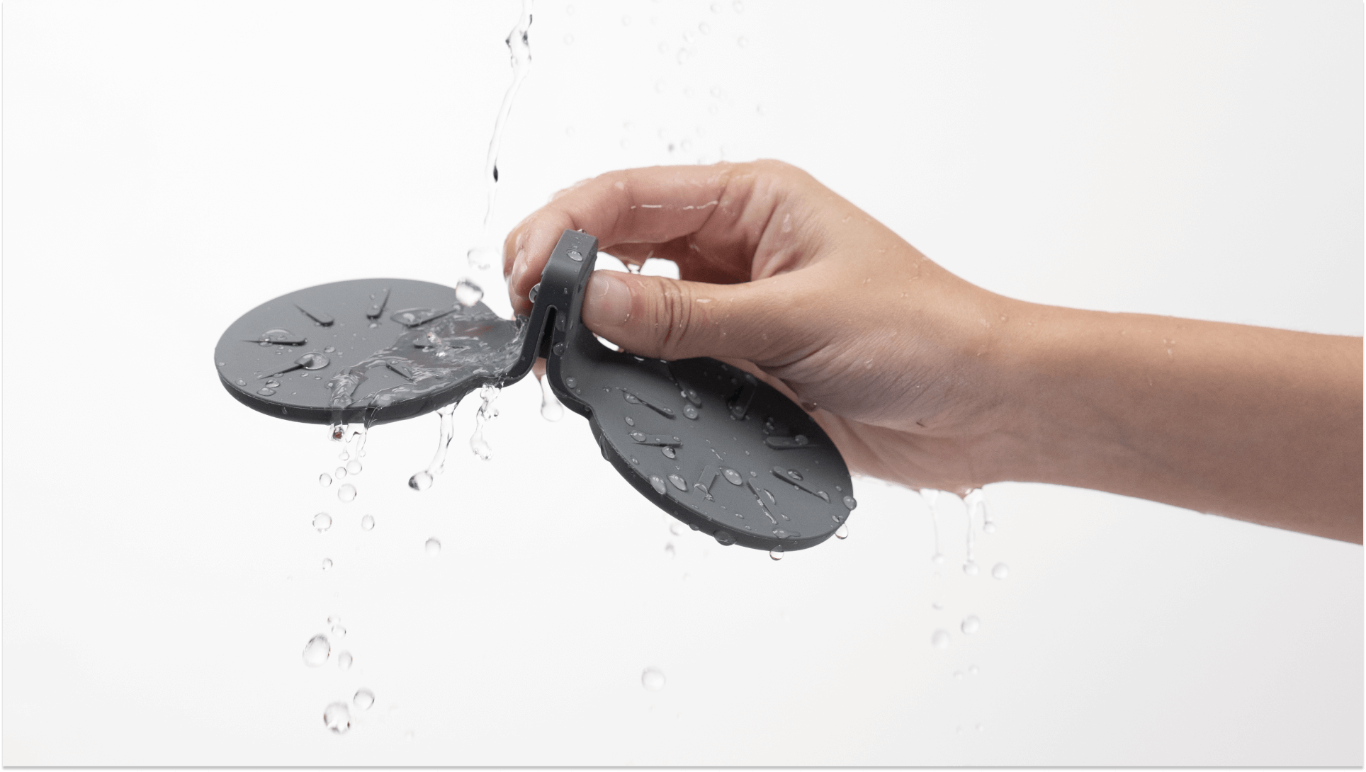 A hand holds a gray, clover-shaped item from the JOWUA Center Console Set designed for Tesla Model S/X against a white background, with water flowing over it to demonstrate its waterproof capabilities.