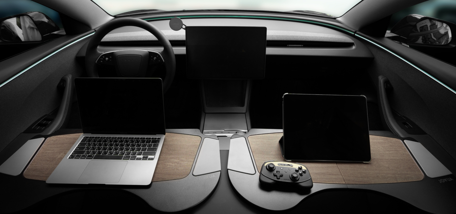 Futuristic car interior showcasing a minimalist design with a steering wheel, two screens on the dashboard, and wooden panels holding a laptop, a tablet, and a gaming controller.