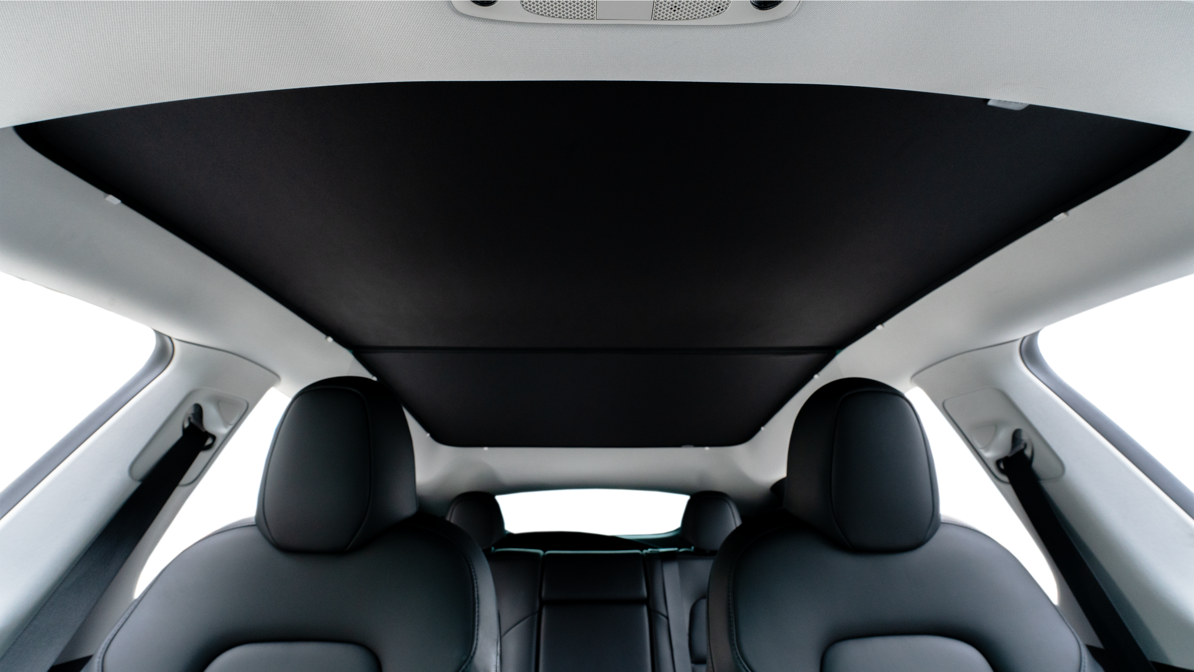 Interior view of a car showing sleek, modern black leather seats and a panoramic glass roof with a sunshade. The overhead console is visible against the light interior ceiling.