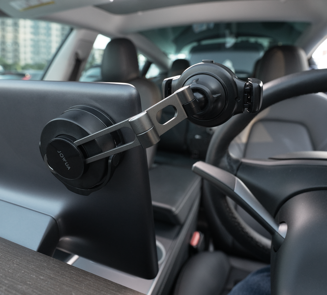 Close-up of a car interior featuring a dual-mount phone holder attached to the center console screen. The car is parked, and a steering wheel is partially visible on the right side of the image.