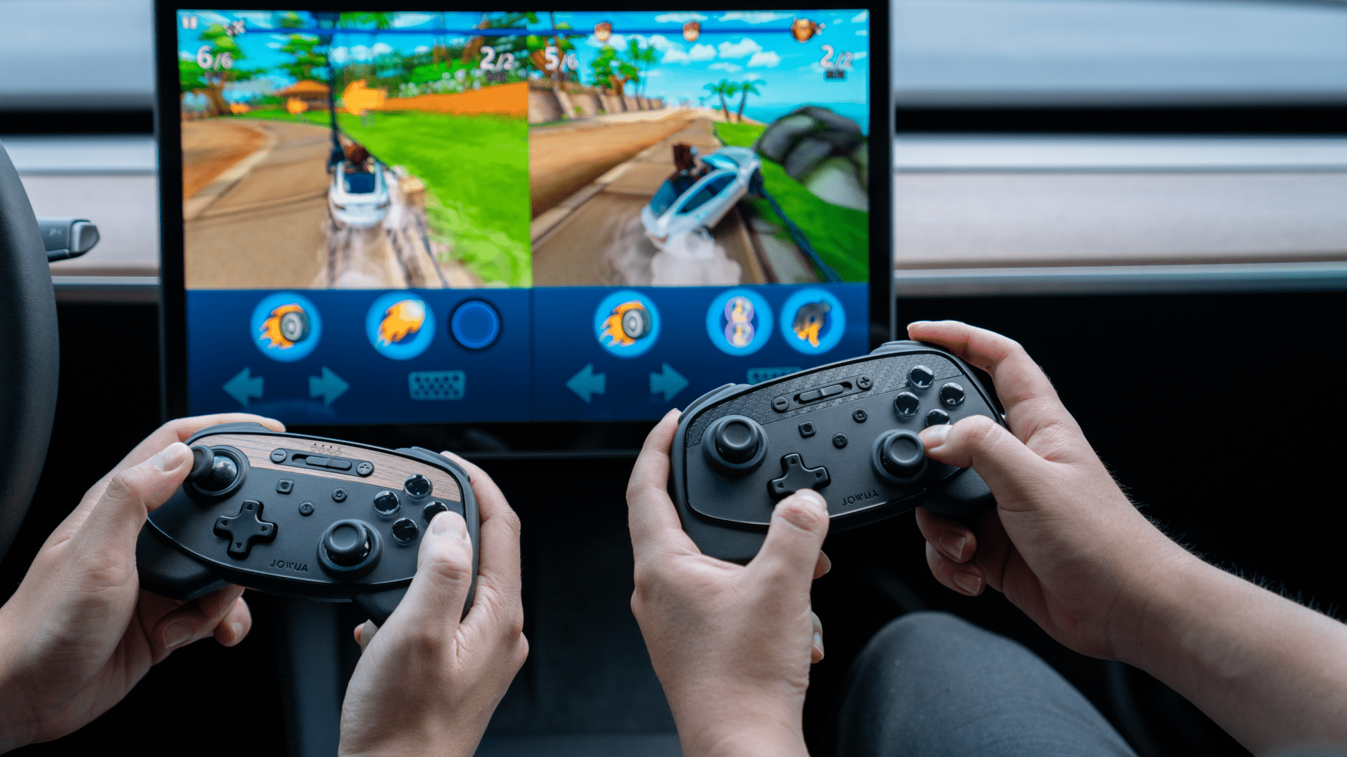 Two people are playing a racing video game on a screen using wireless controllers. The game features split-screen mode, showing off-road vehicles on a track with various power-ups.