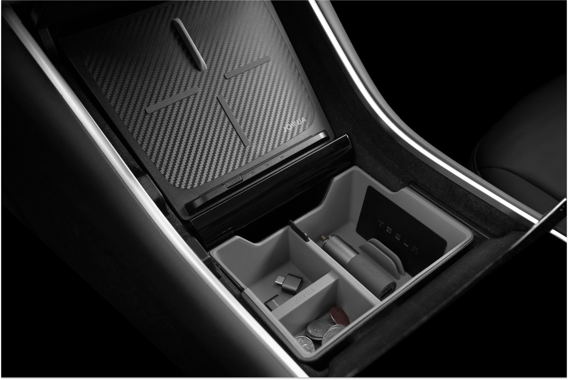Car center console with an organized storage compartment. It has sections containing coins, a charging cable, and other accessories. The lid features a carbon fiber pattern, and the surrounding area is lit with LED lights.