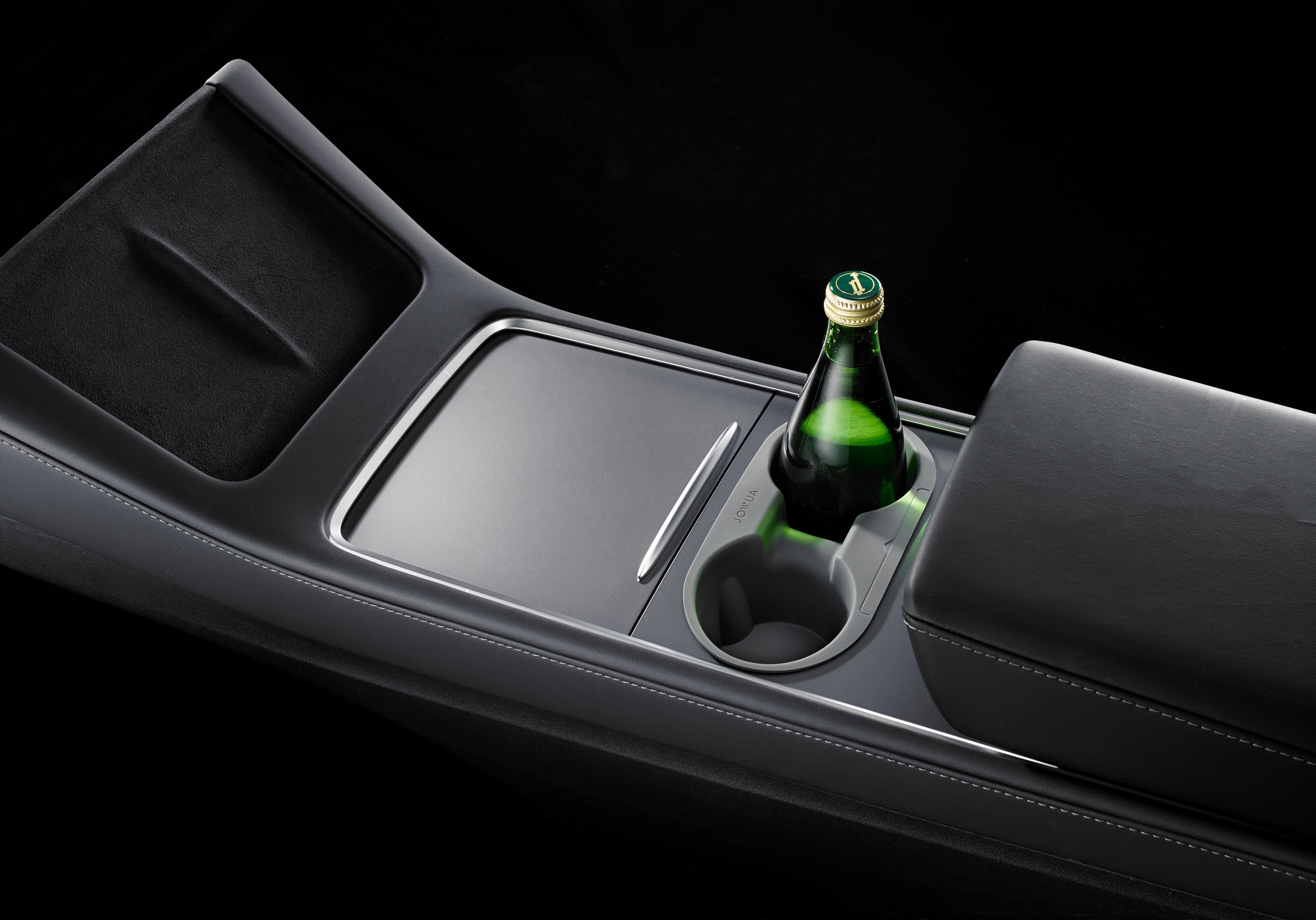 A sleek car center console with a modern design, featuring a cup holder containing a green bottle, a covered storage compartment, and a cushioned armrest.