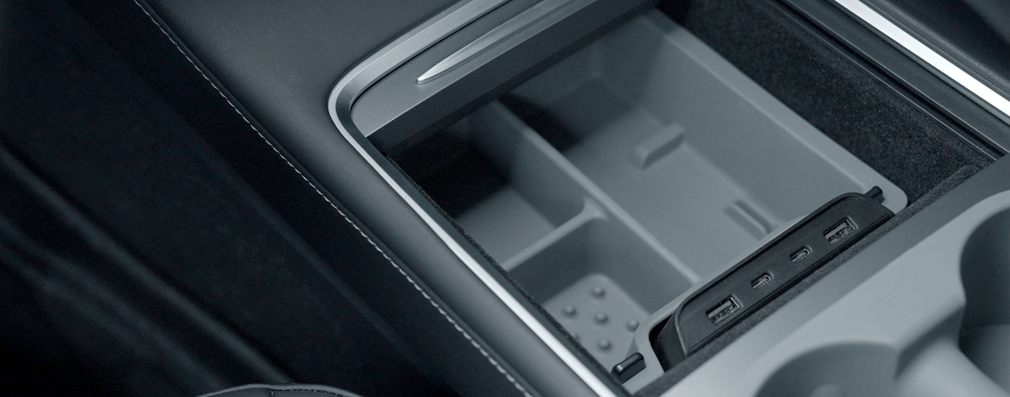 Close-up of a car's center console compartment with multiple dividers and three USB ports, providing storage and charging options. The interior is gray, and the surrounding material is black.