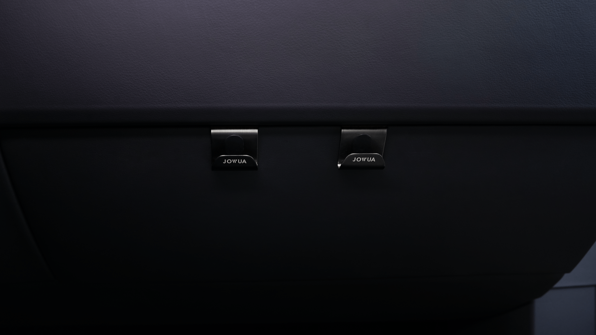 The image showcases two black hooks with a minimalist, modern design. Each hook features "JOWUA," offering easy installation and practicality akin to sleek Tesla glovebox organizers.