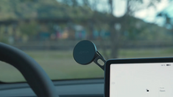 A close-up of a Tesla dashboard shows a circular JOWUA 6D Invisible Foldaway Car Mount Qi2 Wireless Charger (MagSafe) beside the digital display, with a blurred outdoor view through the windshield.