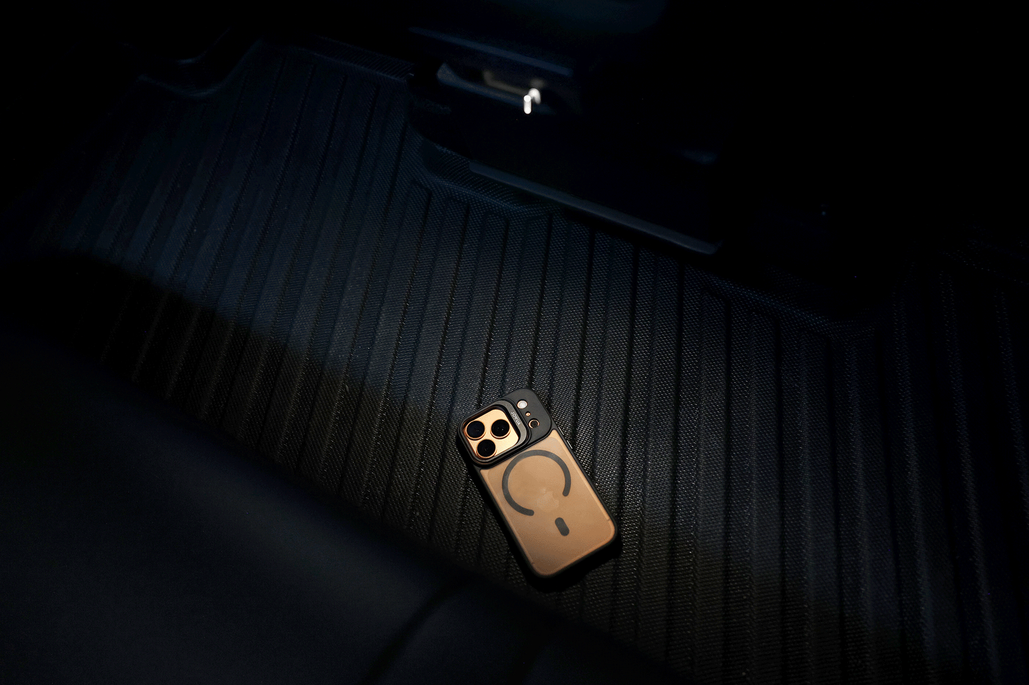 A JOWUA 130W LED Rear Vent Hub (Model 3 Highland 2024+/Model Y Juniper 2025+) casts custom-fit light on a smartphone with dual camera and case resting on the car’s dark, ribbed floor mat, highlighting details in the dim interior.