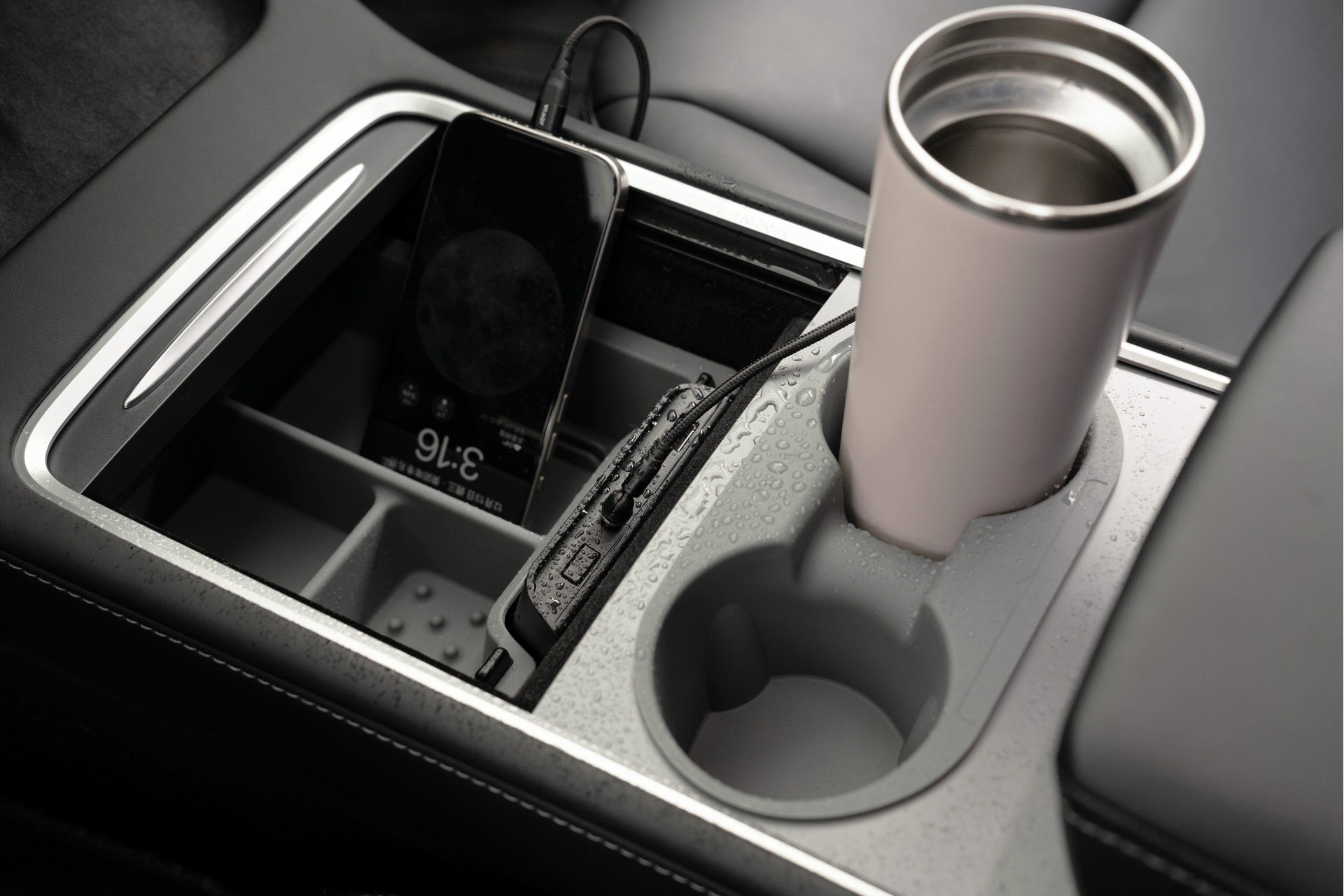 The JOWUA USB Hub for Tesla Model 3/Y, featuring dual USB-C 45W and LED warm light, is connected within a Model 3 center console. A smartphone displays 3:16 on its screen. In the cup holder rests a travel mug, with water droplets shimmering on the console
