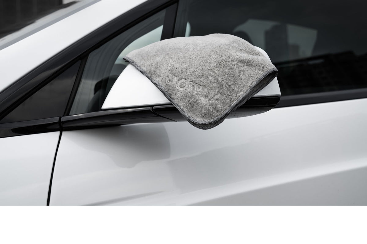 A JOWUA Under Seat Collapsible Organizer & Microfiber Cleaning Cloth Combo is used as a gray cloth rests on a white car’s side mirror, hinting at cleaning or polishing done with essentials stored in the organizer.