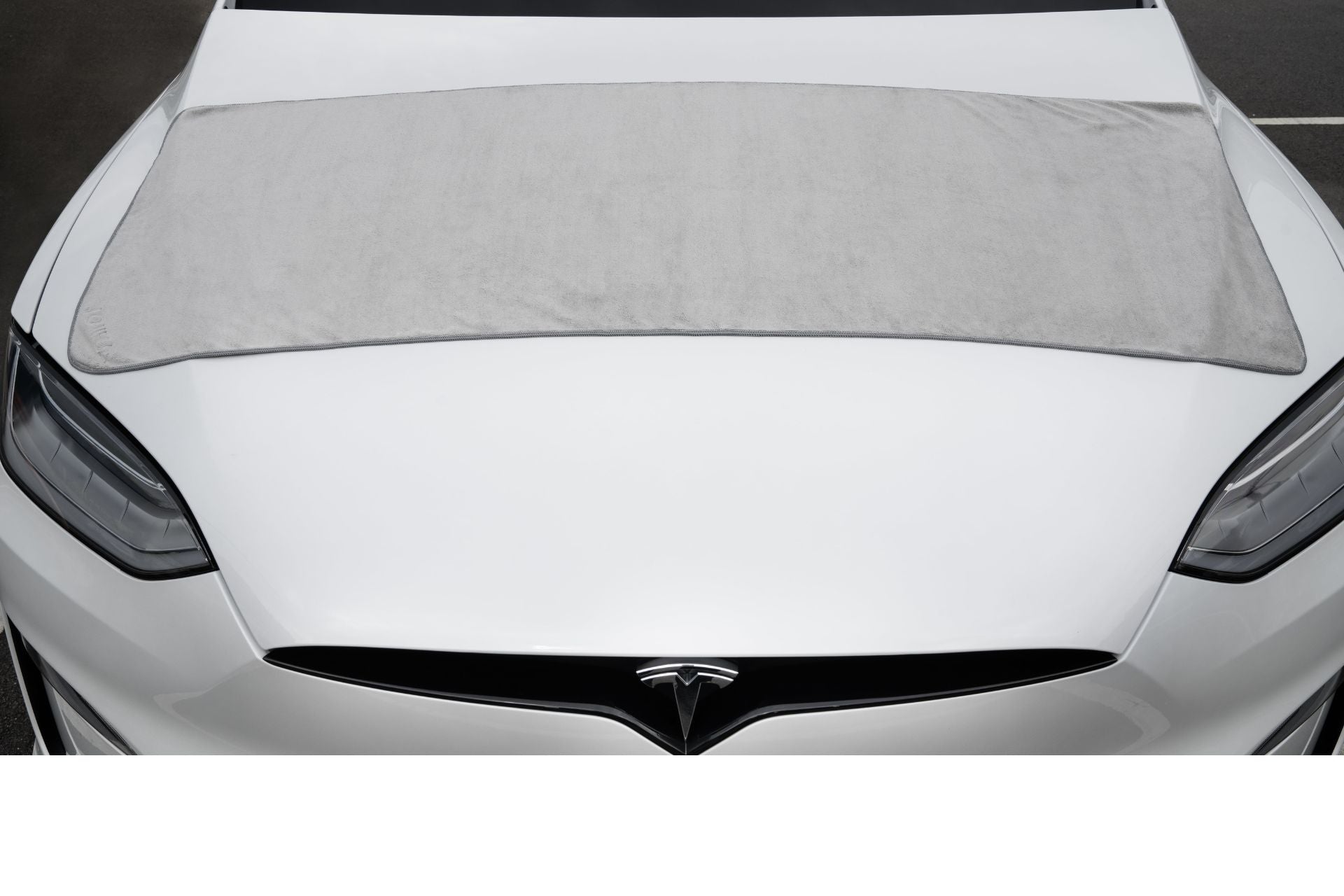 A white car in a parking lot is covered by a gray microfiber cloth from the JOWUA 3 Pack, with its distinct headlights and emblem subtly visible, enhancing its elegance.