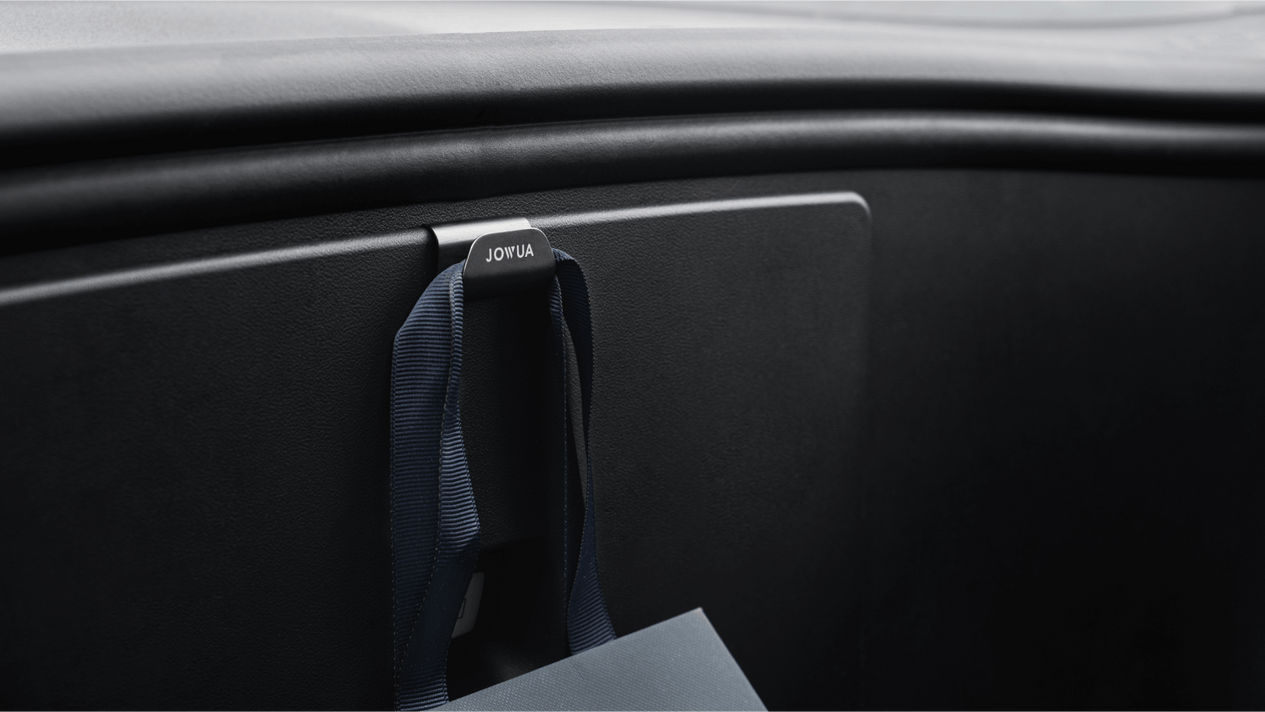 The car dashboard includes a hook labeled "JOWUA," adorned with a blue shopping bag. The chic and contemporary interior of this Model Y highlights a minimalistic design, enhanced by its convenient front trunk storage.