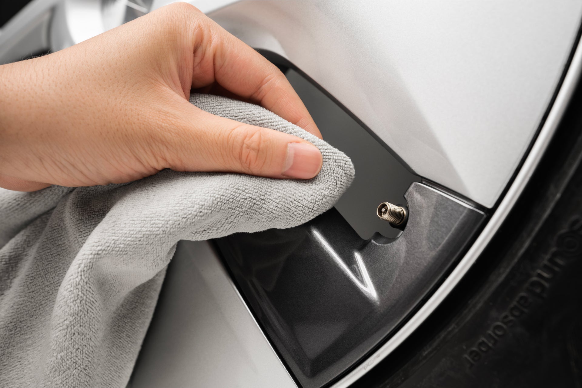 A hand uses a gray cloth to clean the dark gray hubcap of a vehicle