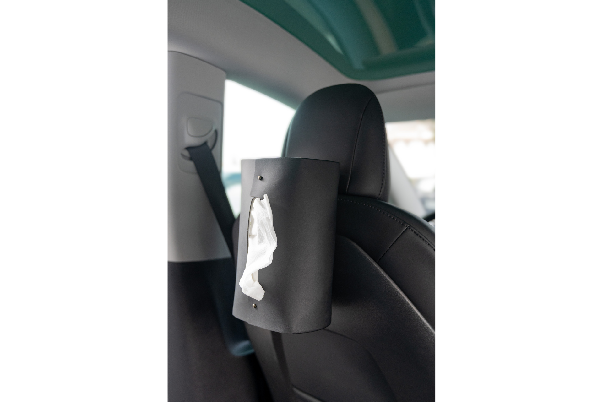 A MagSafe Tissue Box Cover from JOWUA is attached to the back of a Model 3/Y car seat, with a tissue partially pulled out. The interior of the car is visible, showcasing the seat's headrest and a seatbelt.