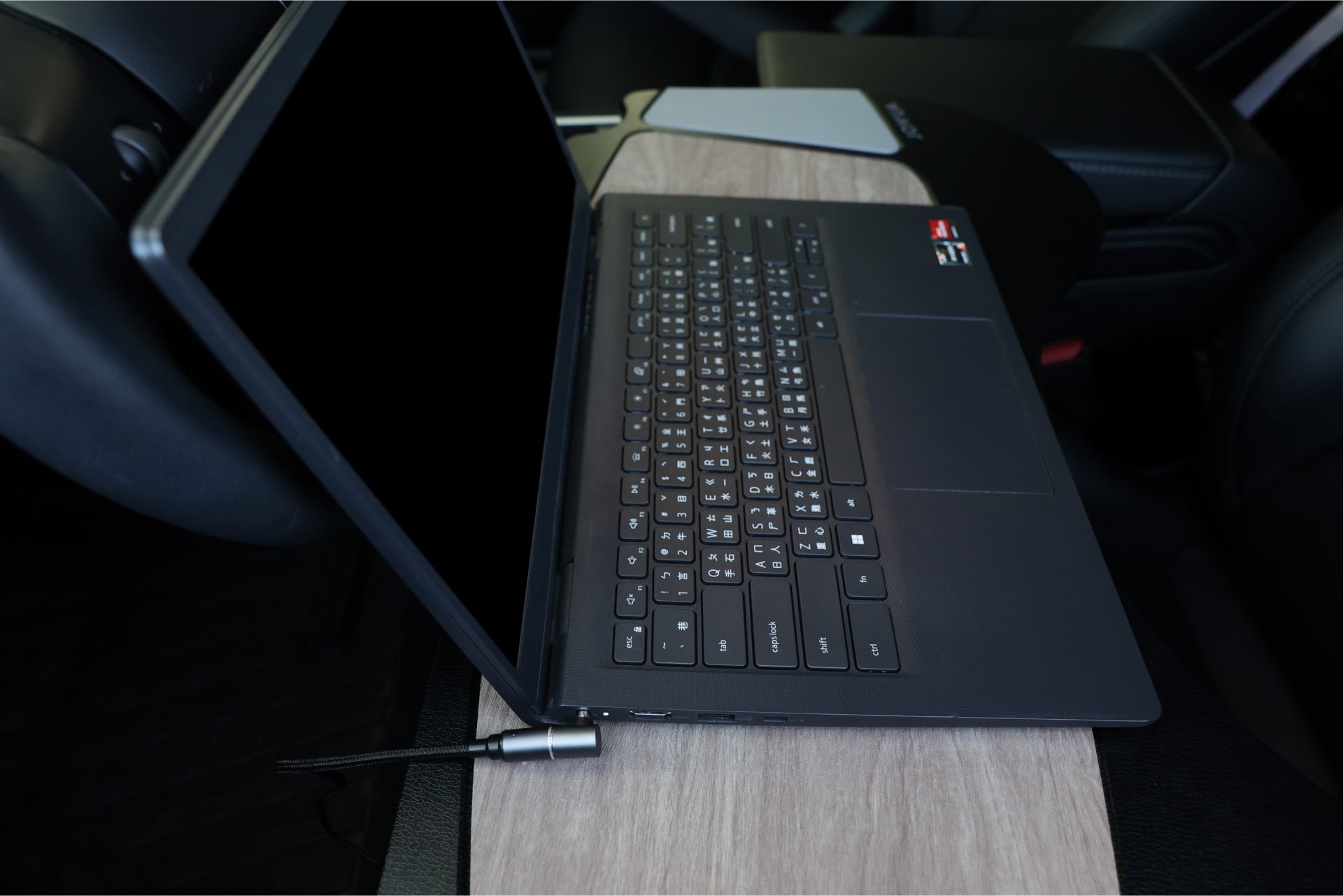 A gray laptop with a black keyboard is open on a wooden surface. Next to it, the JOWUA 100W USB-C to Magnetic DC Charging Cable, boasting a strong magnetic design, is connected via cable. The laptop screen remains black.
