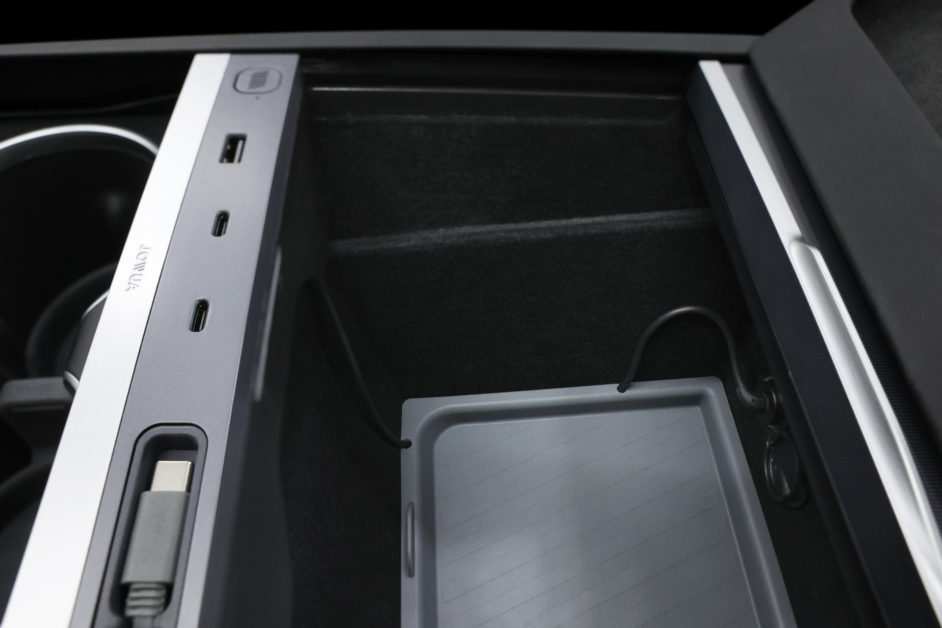 The car's interior boasts a JOWUA 130W LED Hub for Tesla Model Y Juniper 2025+ / Model 3 2024+, featuring multiple charging ports like USB and USB-C. A sleek charging cable connects seamlessly, while a rectangular storage compartment with a removable tray provides efficient charging and storage.