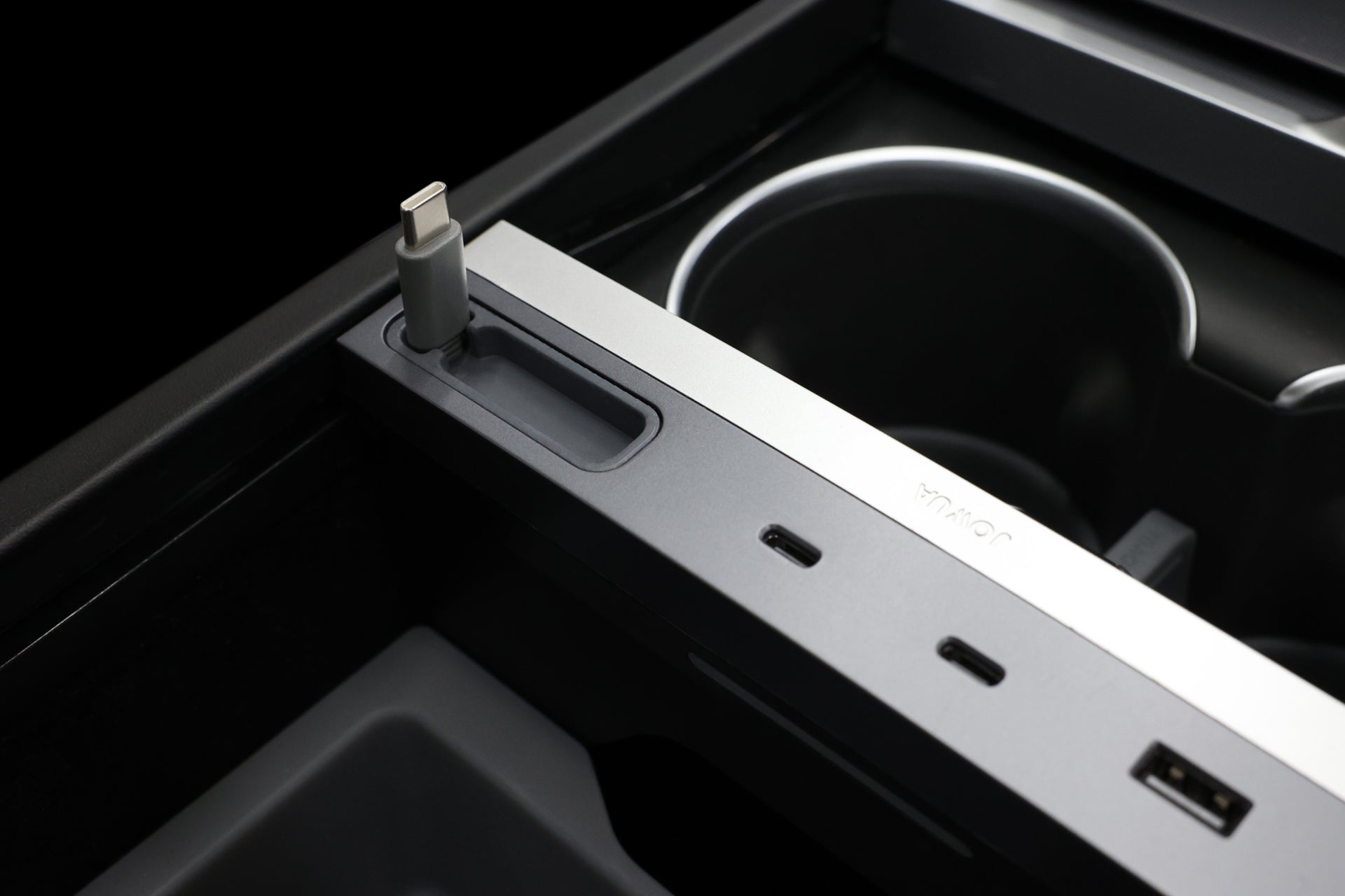 Close-up of the JOWUA 130W LED Hub for Tesla Model Y Juniper 2025+ / Model 3 2024+, showcasing a sleek design with USB-C and USB-A ports. The hub is embedded in a modern, dark setting with visible rounded cup holders.