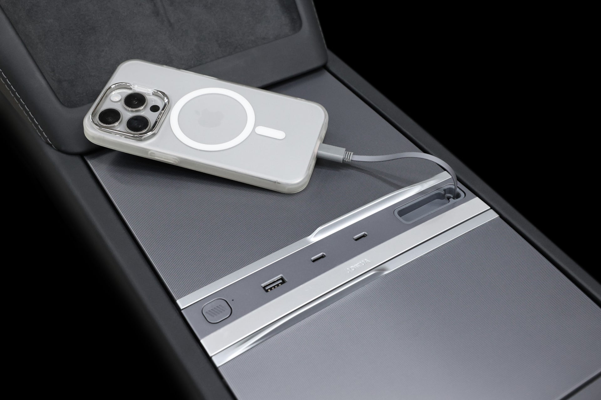 A smartphone with a metallic case and MagSafe ring charges on a Tesla center console using the JOWUA 130W LED Hub for Tesla Model Y Juniper 2025+ / Model 3 2024+, featuring USB ports and a neatly connected cable for efficient charging and storage.