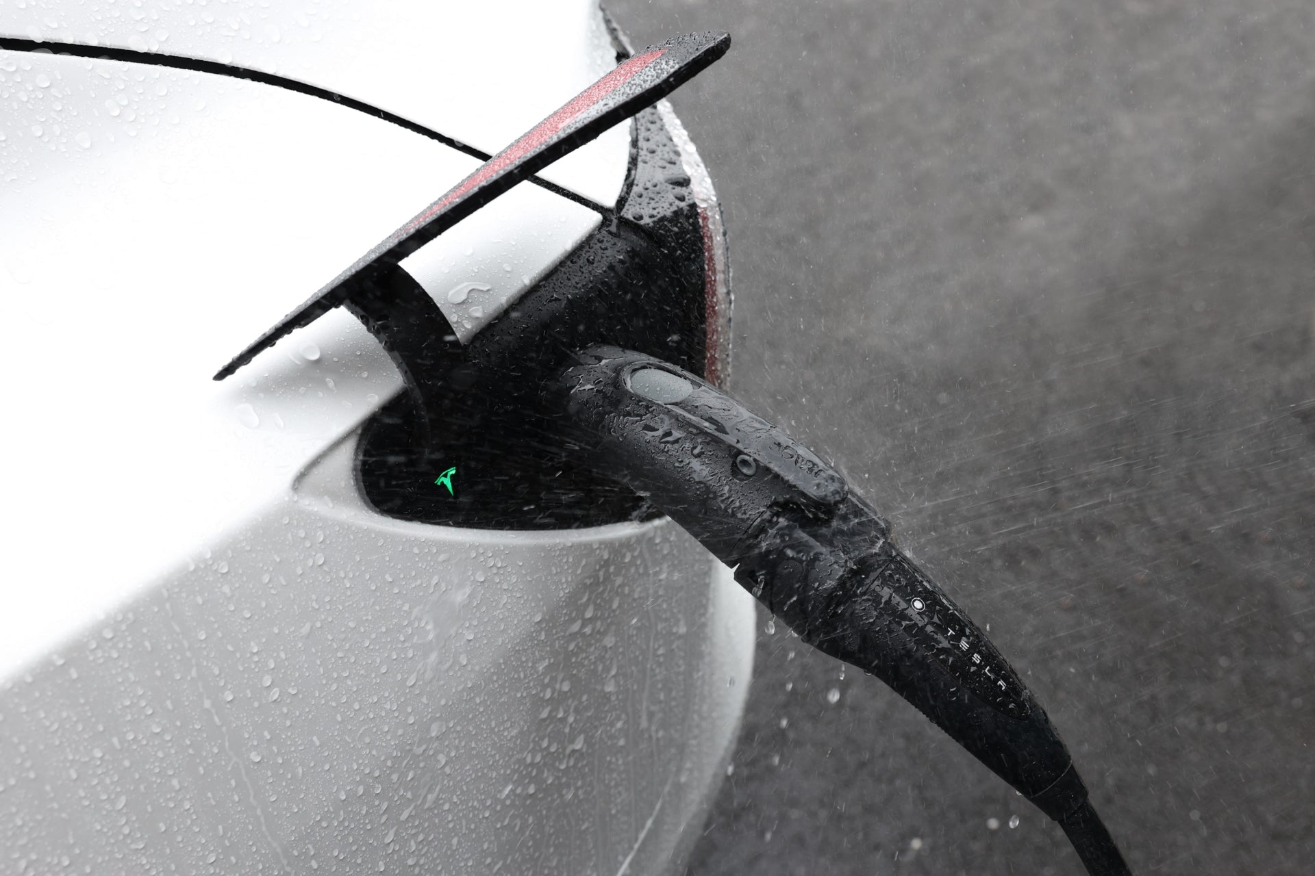 A close-up of a Tesla charging in the rain, with water droplets on the car and cable, connected using the JOWUA CCS2 to NACS DC/AC Charging Adapter Set.