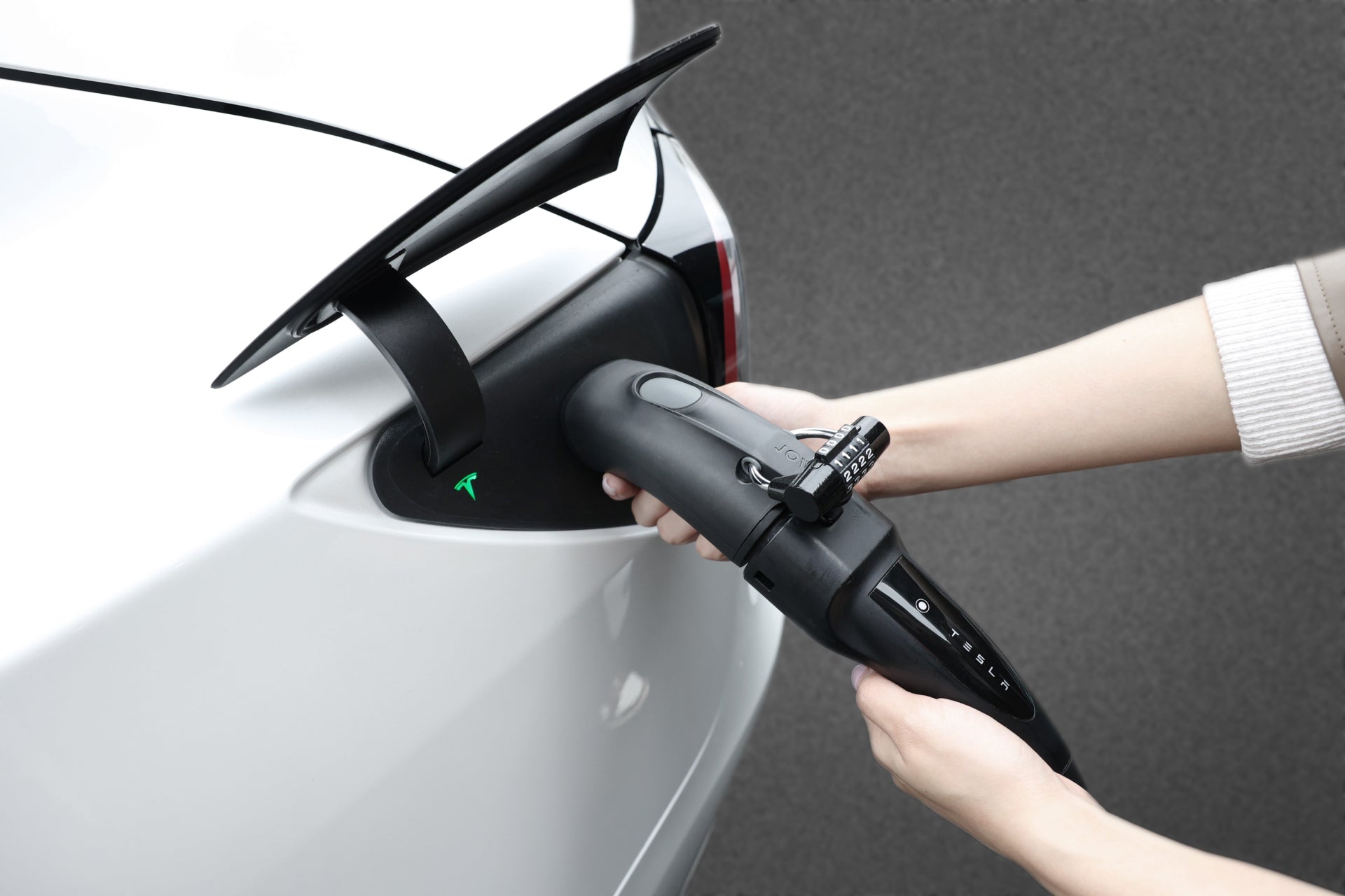 A person plugs a charging cable into a white electric car with the JOWUA CCS2 to NACS DC/AC Charging Adapter Set, preparing to charge the vehicle against a plain gray background.