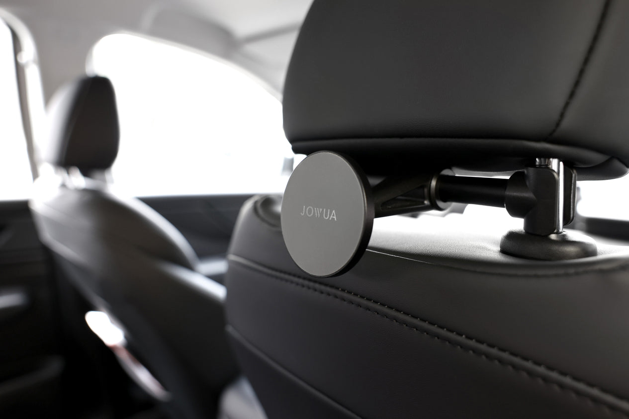 The image displays the JOWUA Universal MagSafe Car Seat Holder mounted on a back seat headrest. This holder features an anti-slip design and is securely attached with adjustable components. The surrounding car interior is modern and sleek, showcasing dark leather upholstery.