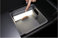 A hand points to a bright rectangular panel inside a ridged gray storage compartment, showcasing the JOWUA Premium Interior Essentials Set for Tesla Model Y Juniper as light illuminates the compartment’s interior.