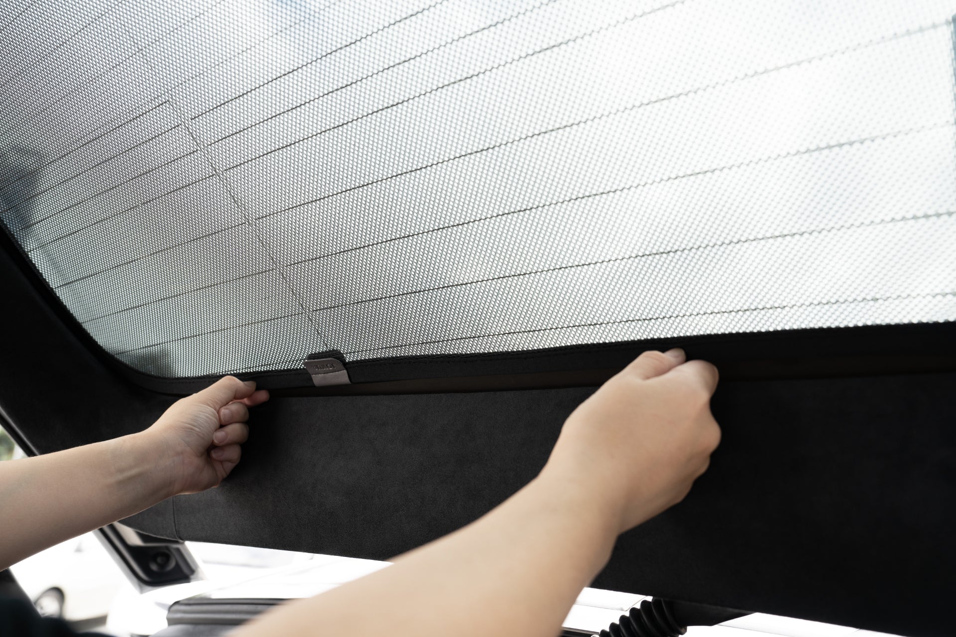 Hands adjust JOWUA's Model X Separate Sunshade Bundle on a rear car window, partially covering the glass. The mesh-like shade allows light while providing privacy and heat insulation. The car's interior, including window lines and trim, is visible.