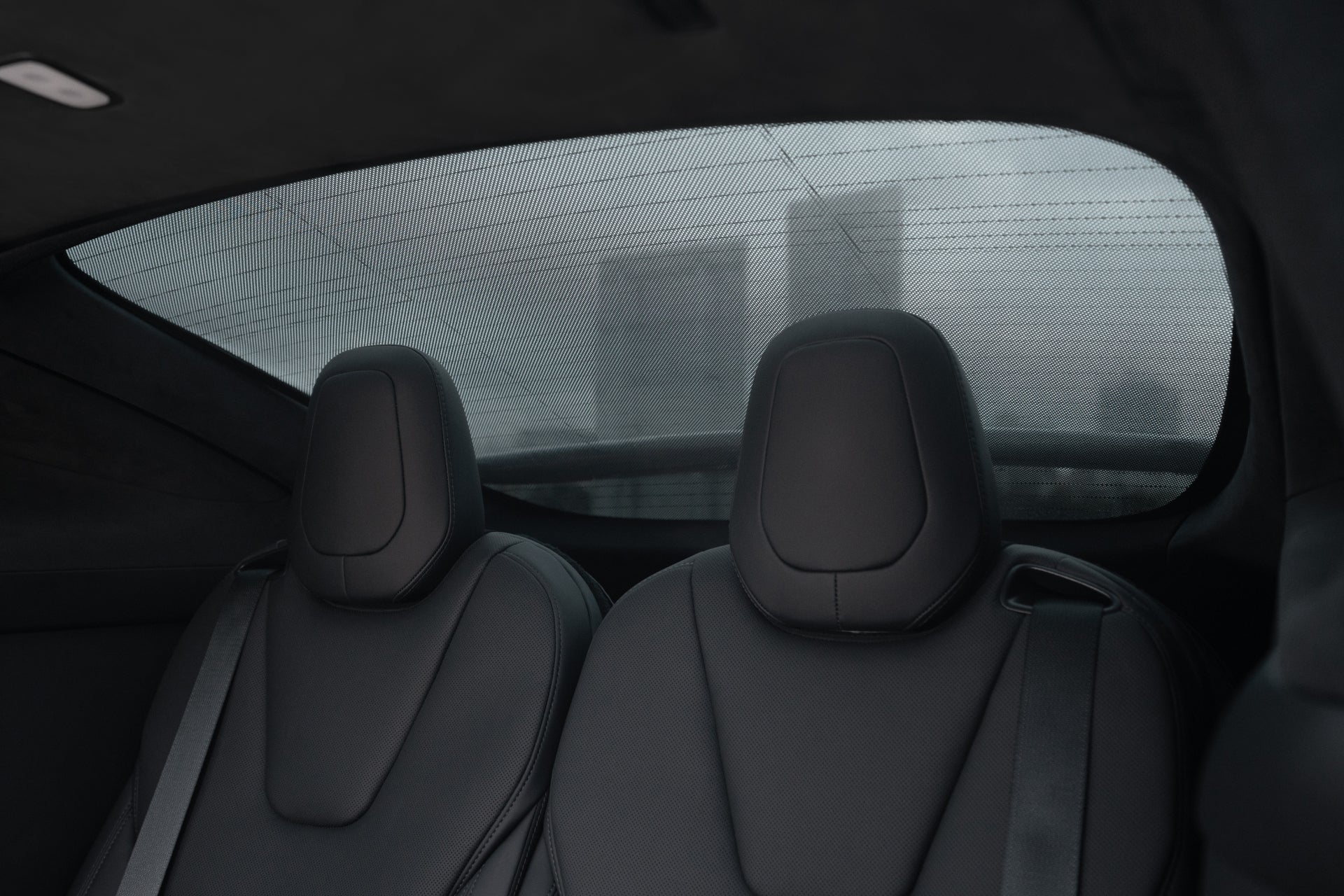The interior of a car shows two unoccupied black leather rear seats, framed by the JOWUA Model X Separate Sunshade Bundle for custom-fit heat insulation. A foggy cityscape with faint building outlines is visible through the rear window, enhancing this serene scene.