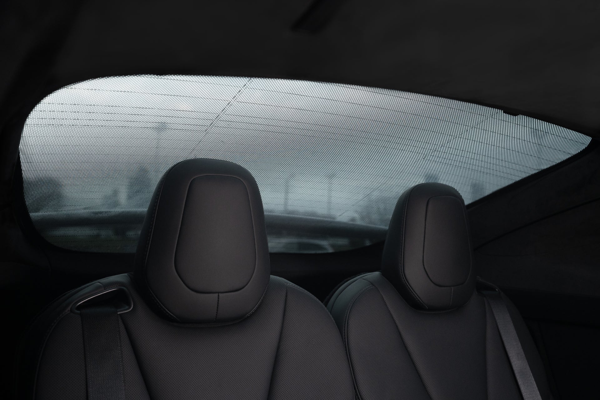 The interior view of a car's backseat features two black leather headrests, with trees faintly visible through the rear window. The fogged glass suggests an overcast day, while the JOWUA Model X Separate Sunshade Bundle boosts heat insulation for added comfort.