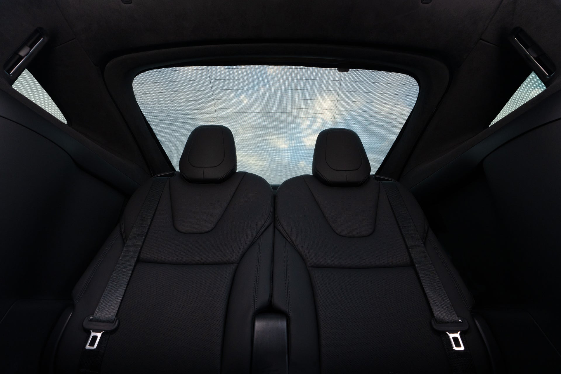 The image highlights the backseat area of a car, showcasing two black seats crafted from high-density woven fabric. A JOWUA Rear Lift Gate + Triangular Window Sunshade for Model X is visible on the large rear window, revealing a glimpse of a partly cloudy sky.