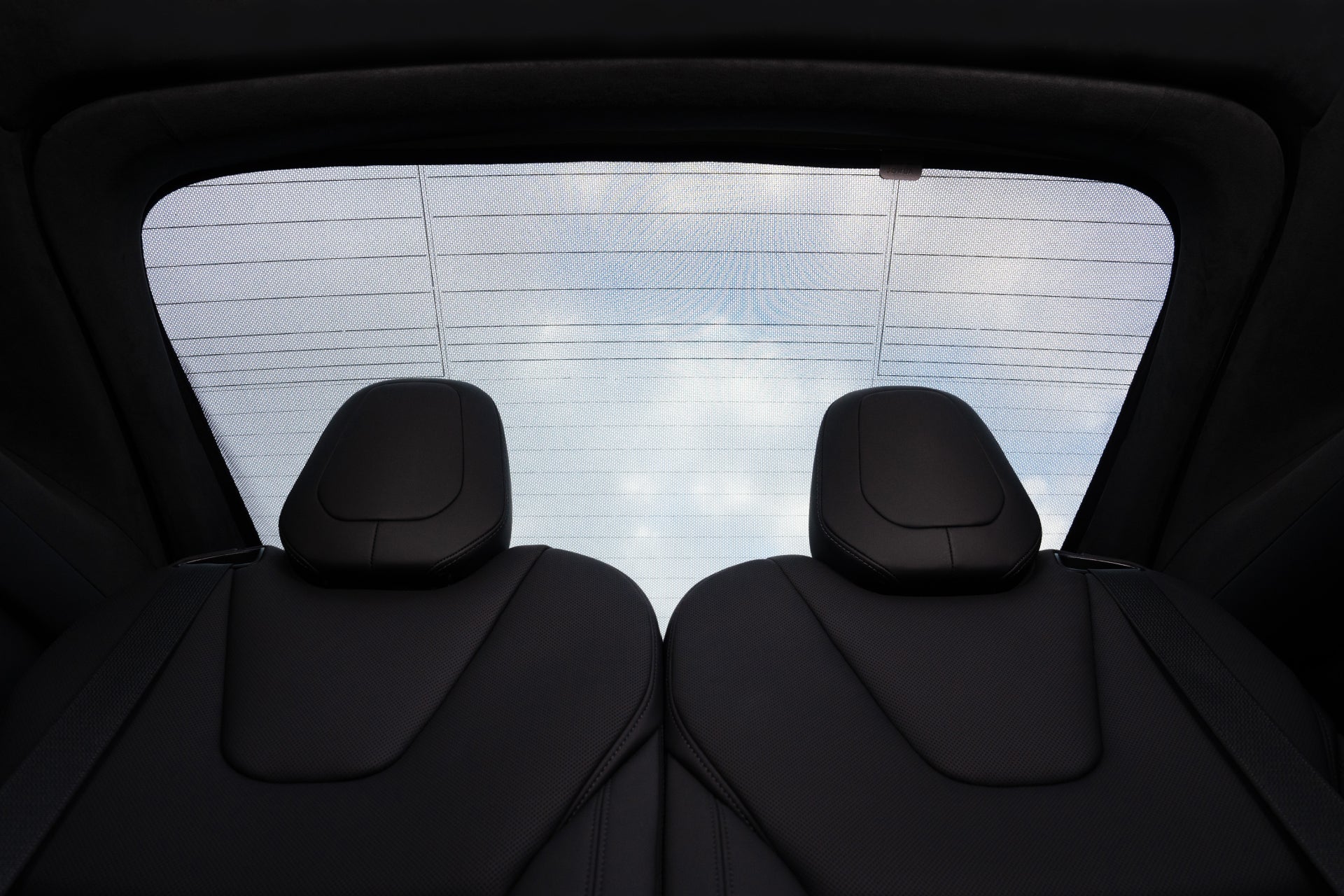 Through the rear window of a car, the cloudy sky looms, casting light over two silhouetted headrests. The JOWUA Model X Separate Sunshade Bundle provides custom-fit insulation, gently shading this tranquil scene.