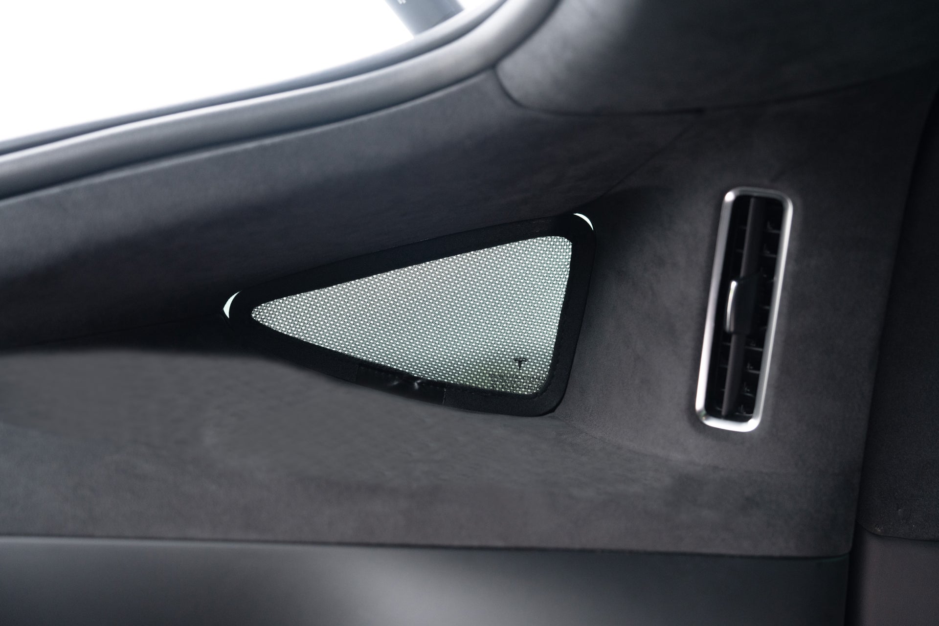 Close-up of a car's interior showing a triangular mesh window with JOWUA's Model X Separate Sunshade Bundle for top-notch heat insulation, alongside a sleek right air vent. The smooth, dark fabric lining highlights its modern minimalist design.