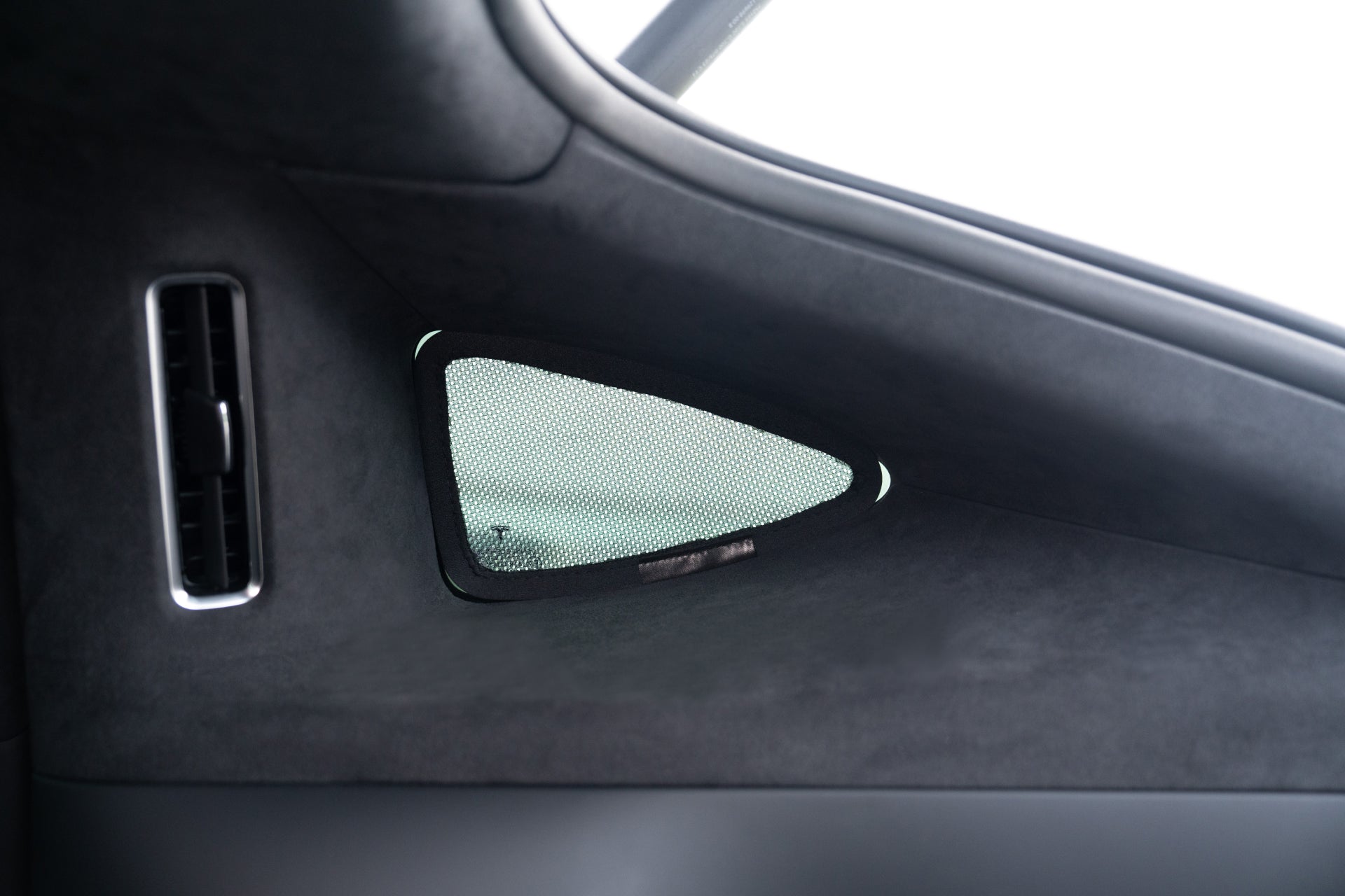 Close-up of a car's interior shows a triangular mesh panel by the vertical air vent. The sleek design is enhanced with the JOWUA Model X Separate Sunshade Bundle, offering heat insulation while bright light filters in.