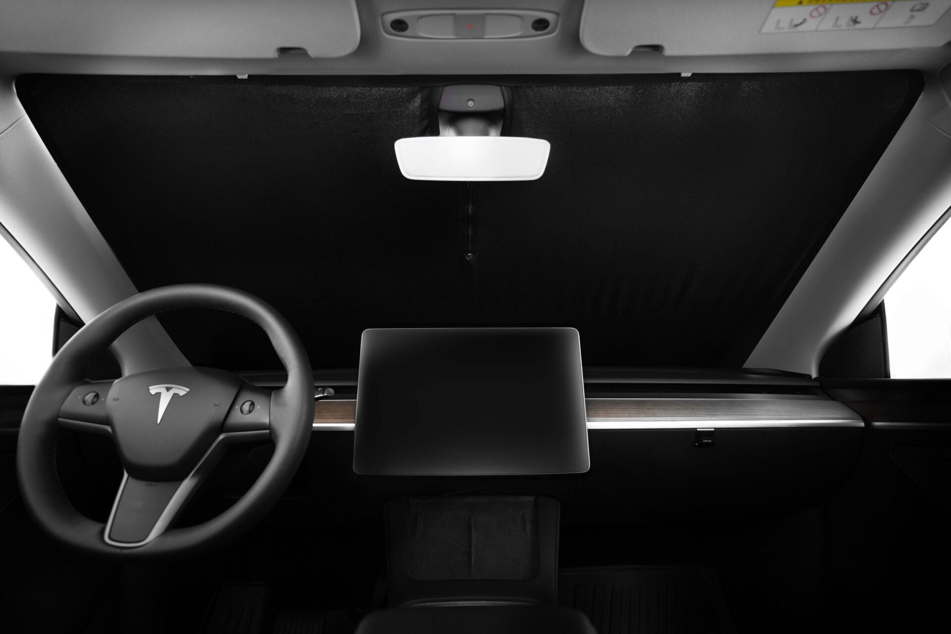 The interior of this electric car features a sleek, minimalist dashboard with a large touchscreen set on a wooden strip. A steering wheel adorned with the JOWUA logo and the Windshield Sunshade for Model Y provide UV protection, while the rearview mirror contrasts against the dark windshield covering.