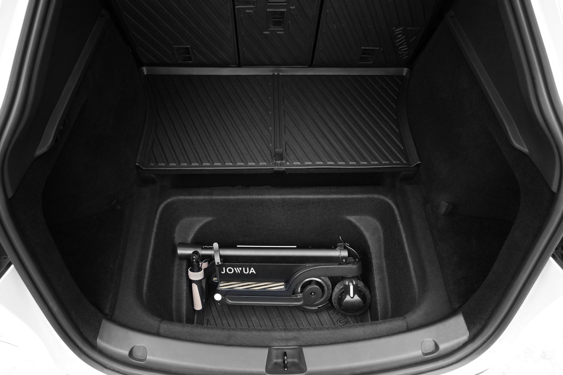 A folded black electric scooter with white handles sits in a Tesla Model Y trunk, which is protected by the JOWUA Model Y EasyShield Waterproof Trunk Liner + Rear Seats Back Cover Bundle (Juniper 2025+/2018-2024).