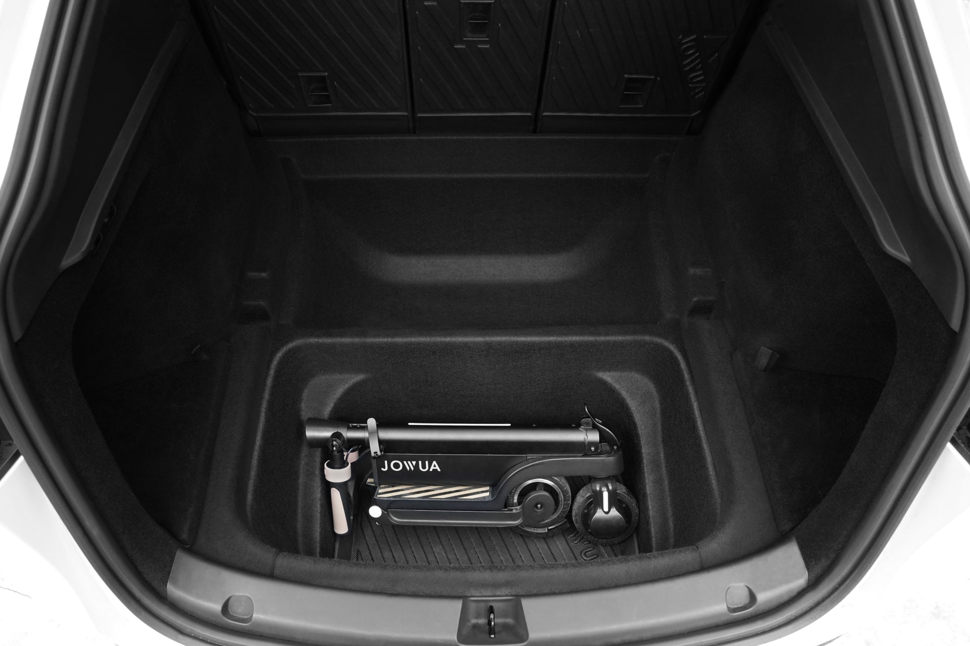 A black and white foldable electric scooter rests on the JOWUA Model Y EasyShield Waterproof Trunk Liner + Rear Seats Back Cover Bundle (Juniper 2025+/2018-2024), with the rear seats of the Tesla Model Y in view.