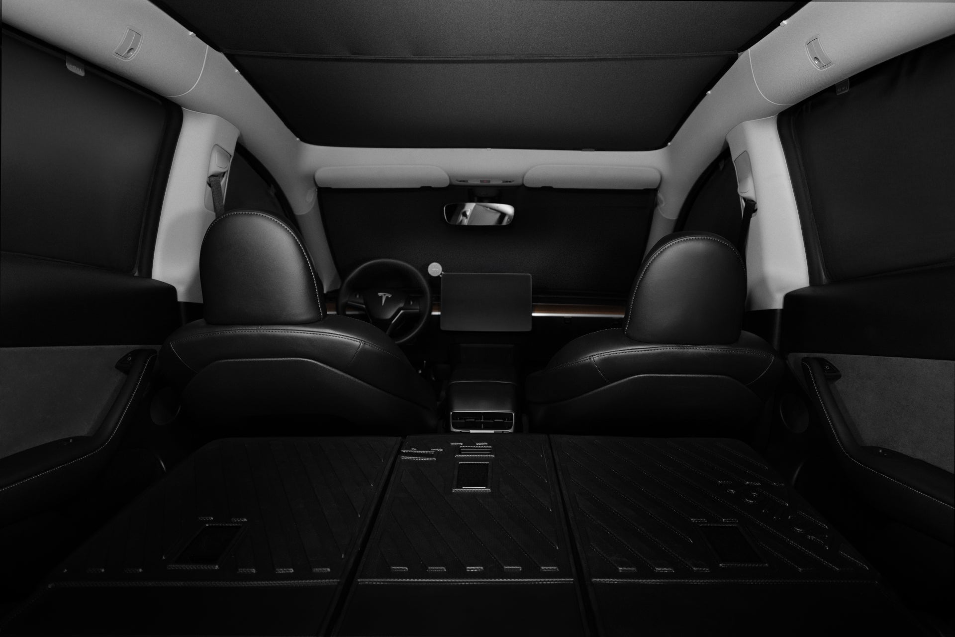 The interior of the car features sleek black leather seats, a large touchscreen dashboard, and a branded steering wheel. A JOWUA Model Y Ultimate Sunshade Bundle in Dark Matter mesh fabric offers UV protection overhead. With the back seats folded down, the spacious cargo area is revealed, showcasing a modern and stylish design.