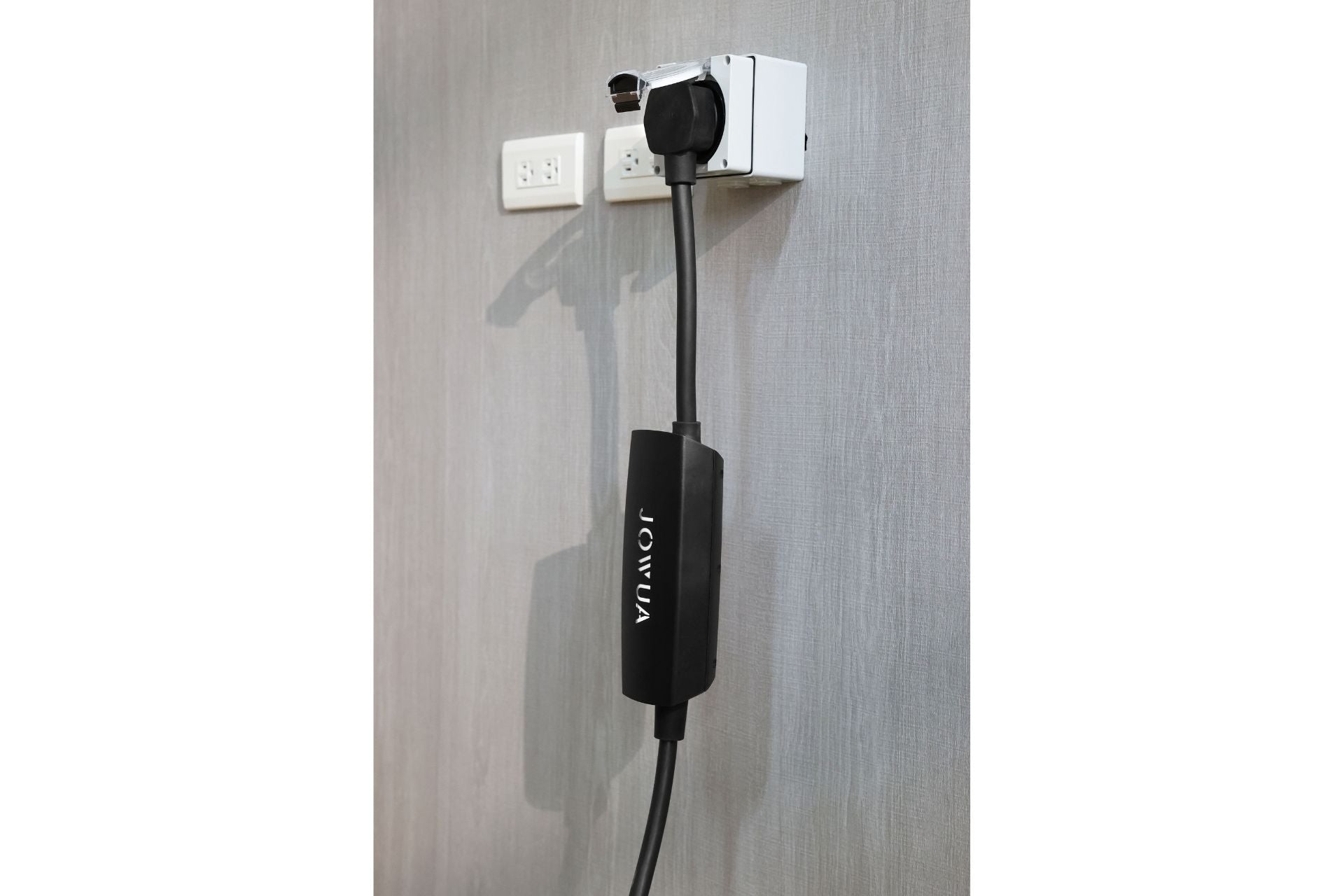 A black "JOWUA" branded power adapter, ETL Listed for safety, is plugged into a white NEMA 14-50 Weatherproof Power Outlet Box with three sockets. The outlet is mounted on a gray wall, and the adapter