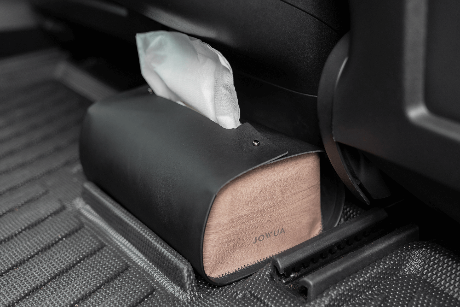 A black leather rectangular tissue holder with a wooden base and the "JOWUA" brand name is positioned on the Model 3 All-Weather Floor Liners inside a Tesla Model 3. A tissue extends from the holder, seamlessly matching the car's custom-fit textured flooring design.