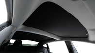 View of a JOWUA Reengineered Model 3 Glass Roof Sunshade (US Version) interior from the back seat, highlighting a dark panoramic sunshade. The roof lining is light-colored and provides UV protection, with the seats partially visible.