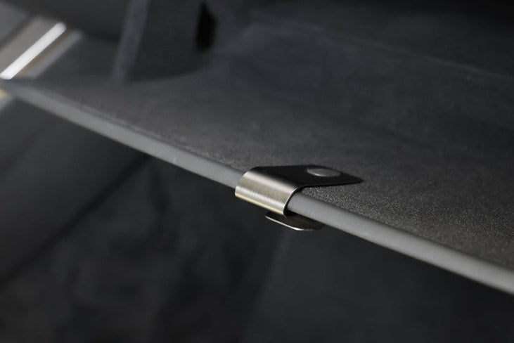 Close-up of a metal clip securing a dark, textured panel from the JOWUA Premium Interior Essentials Set – Model Y Juniper, with a blurred black background.