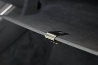 Close-up of a metal clip securing a dark, textured panel from the JOWUA Premium Interior Essentials Set – Model Y Juniper, with a blurred black background.