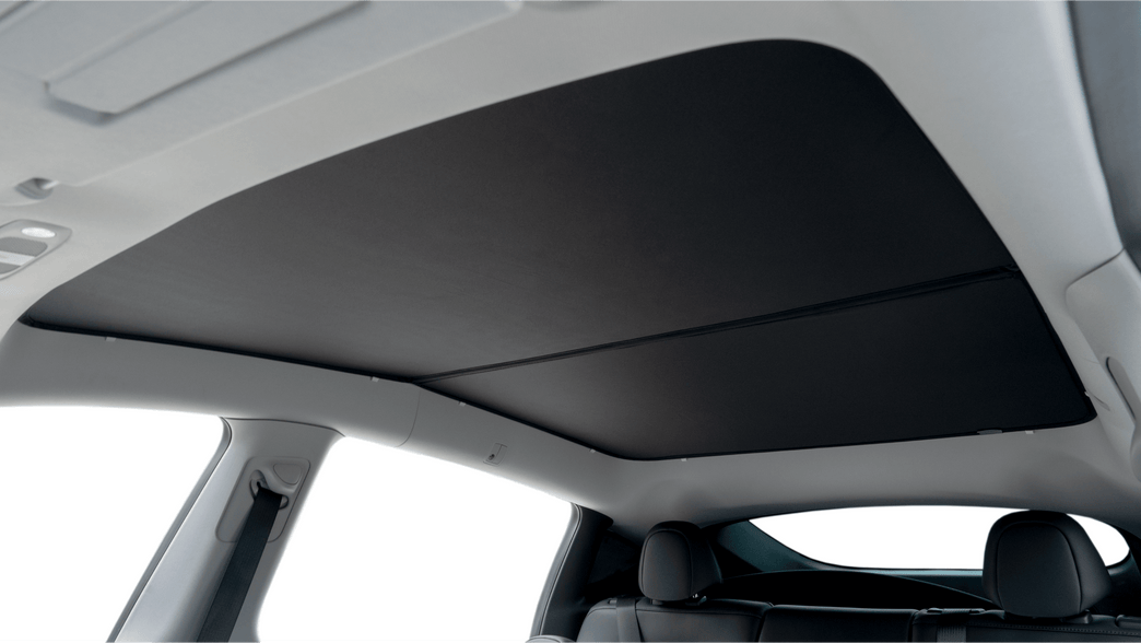 Interior view of a car with a JOWUA All Model Y Glass Roof Sunshade (Juniper 2025+ / 2021-2024), featuring a black mesh fabric cover partially shading the panoramic window for UV protection. The frame is light-colored, and seats are visible in the image's lower part.