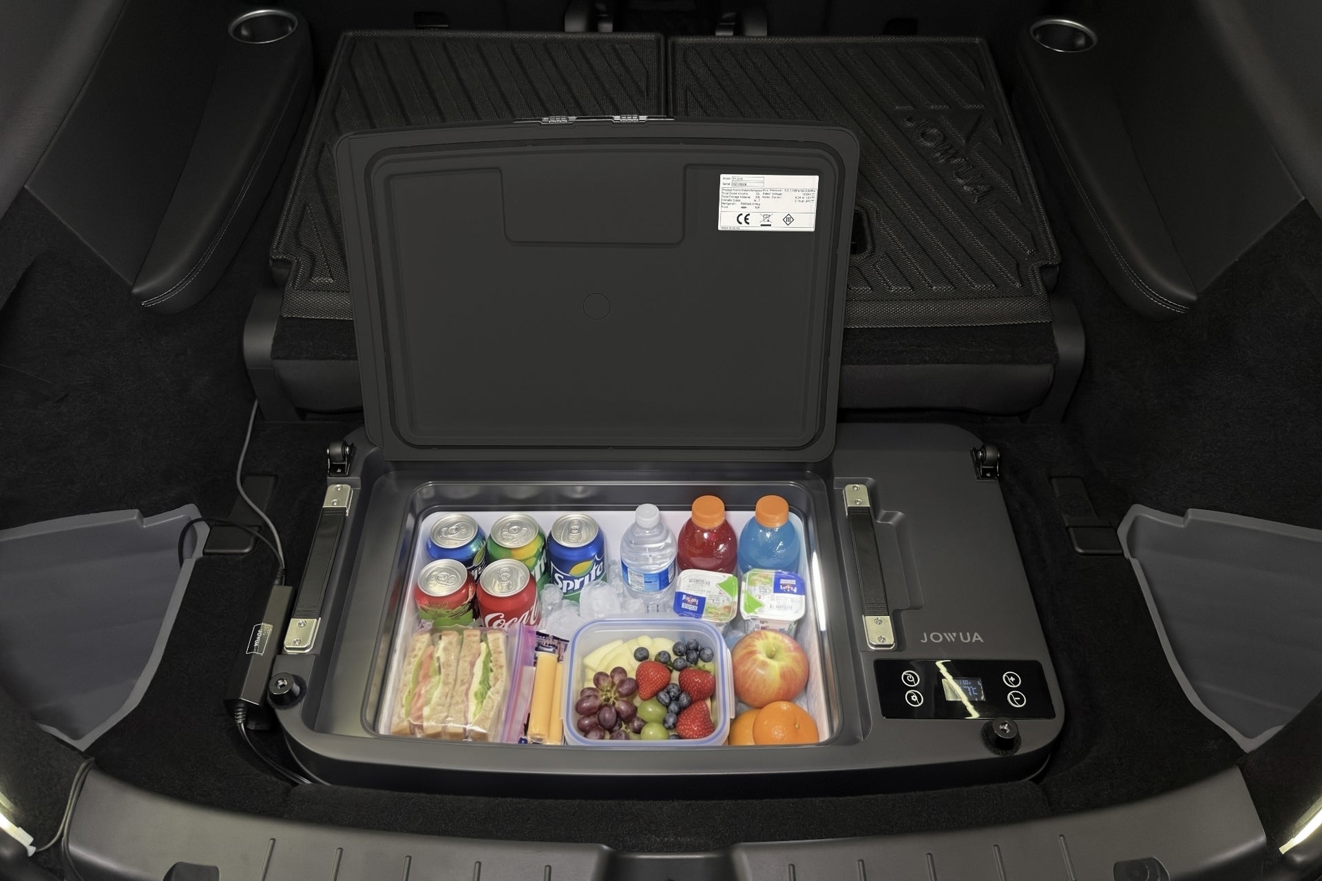 A JOWUA Car Refrigerator for Tesla Model Y L (2026+) with intelligent dual-mode cooling installed in a vehicle trunk, filled with assorted canned drinks, water bottles, fruit, and snacks.