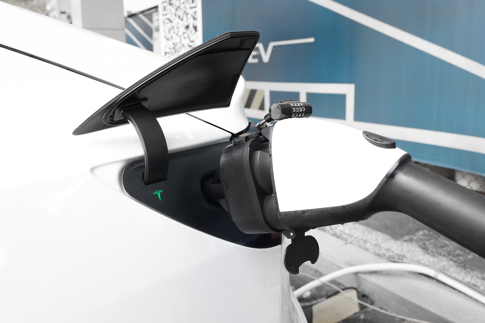 A close-up of a white Tesla being charged using a JOWUA CCS1 to NACS DC & AC Charging Adapter, with the cable plugged in and the Tesla logo clearly visible.