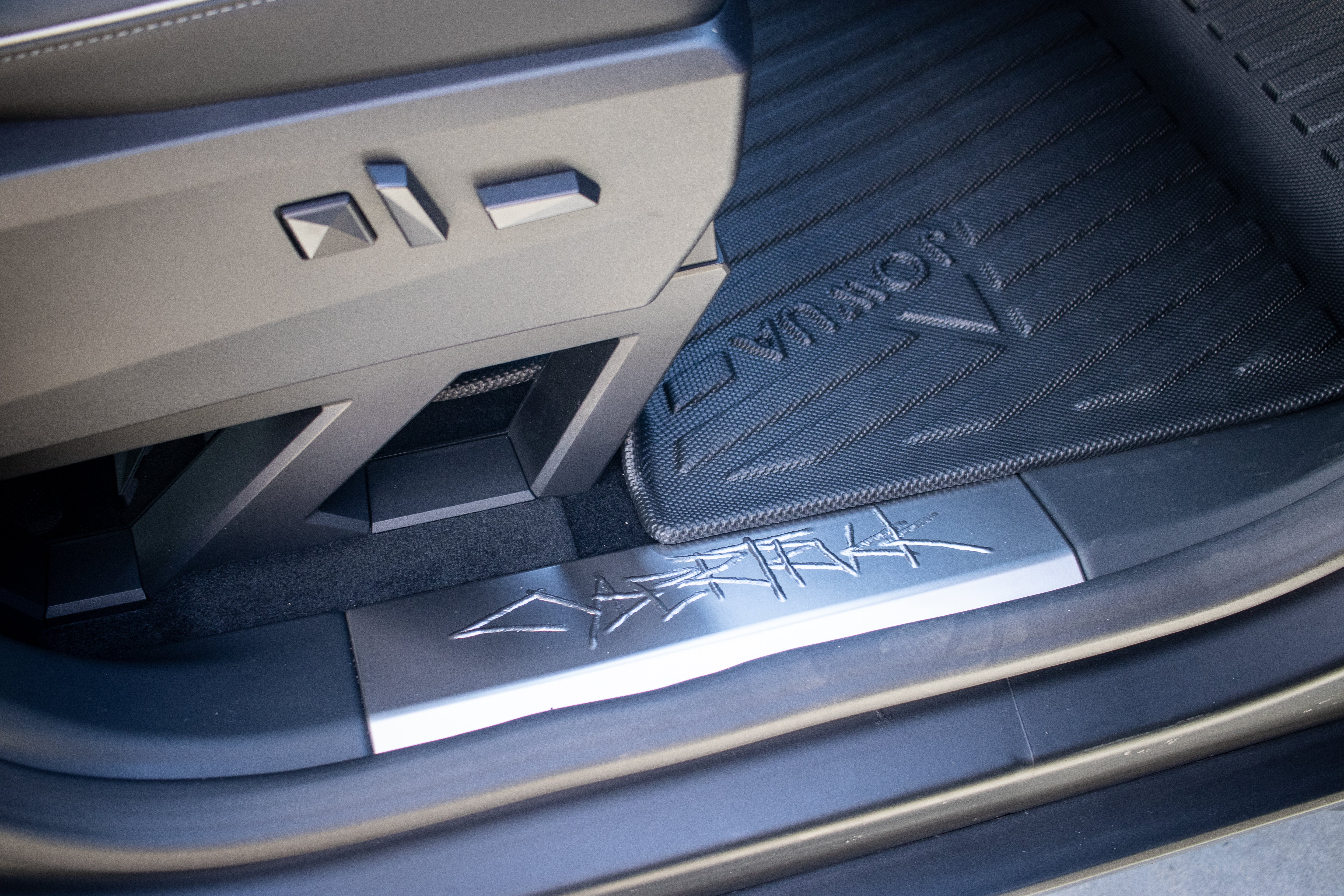 A close-up of JOWUA's All Weather Floor Liners for the Tesla Cybertruck showcases metallic accents and geometric shapes, including the word "HYBRID." Angular designs enhance the interior door sill panel.