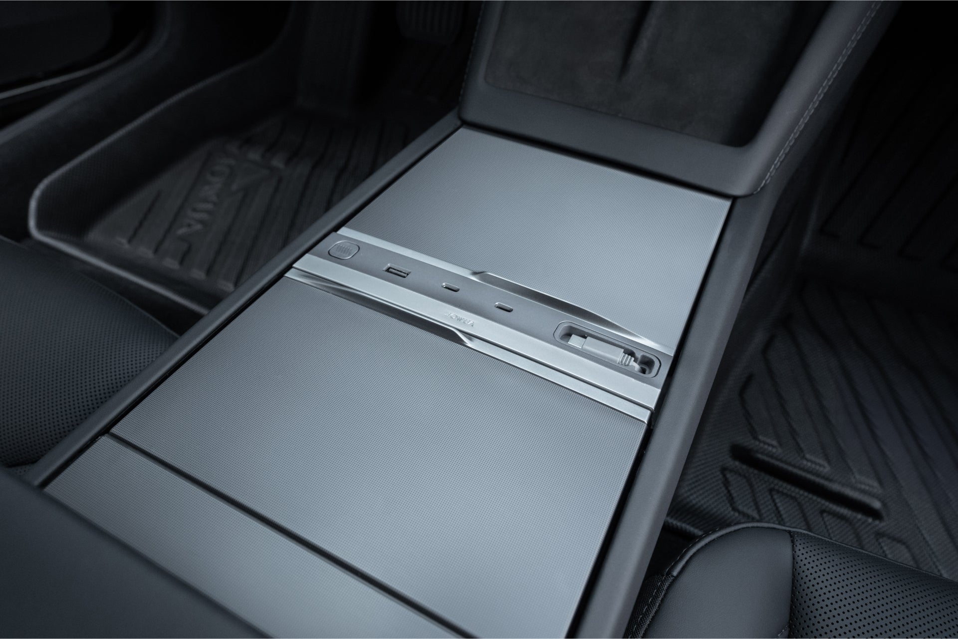 Close-up of a Tesla center console featuring the JOWUA 130W LED Hub for Model Y Juniper 2025+ / Model 3 2024+, with sliding metallic cover, USB ports, cupholder area, sleek black interior, and textured floor mats.