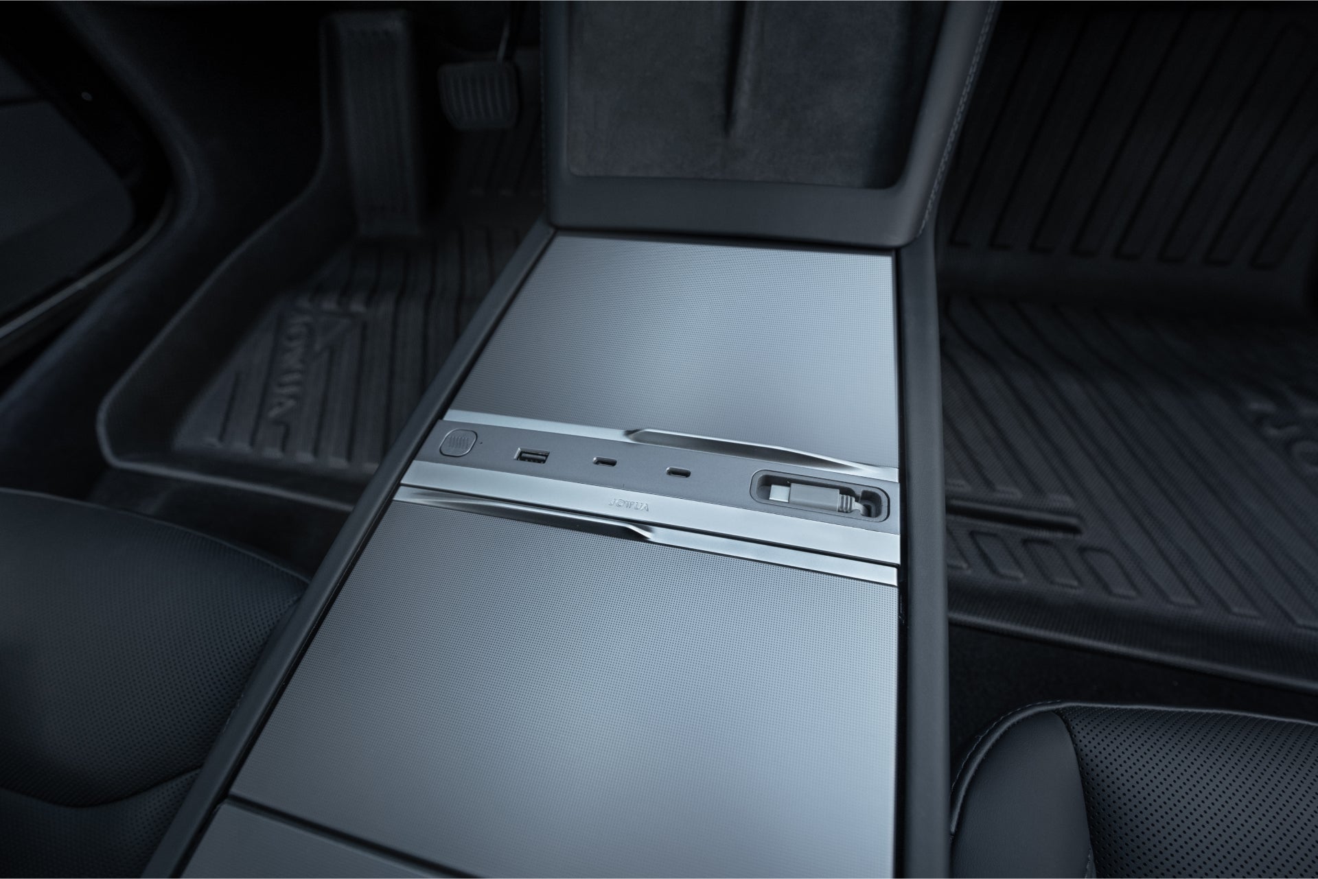 Close-up of a JOWUA 130W LED Hub for Tesla Model Y Juniper 2025+ / Model 3 2024+ on the car’s center console, with sleek metallic surfaces, USB ports, black molded floor mats, and part of the seats visible.