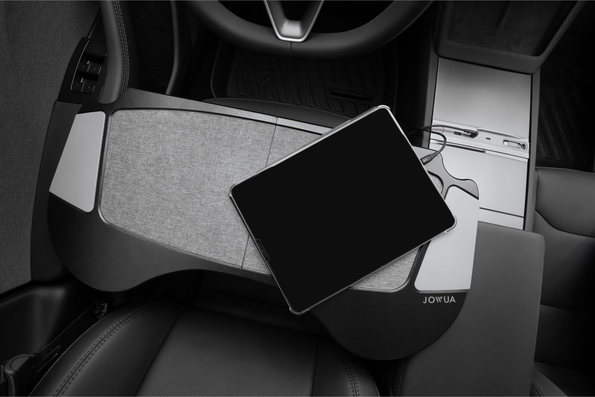 A tablet sits on a gray, fabric tray over the steering wheel in a Tesla. This JOWUA 130W LED Hub for Model Y Juniper 2025+ / Model 3 2024+ provides easy access, complementing the sleek interior with leather seats and advanced controls.