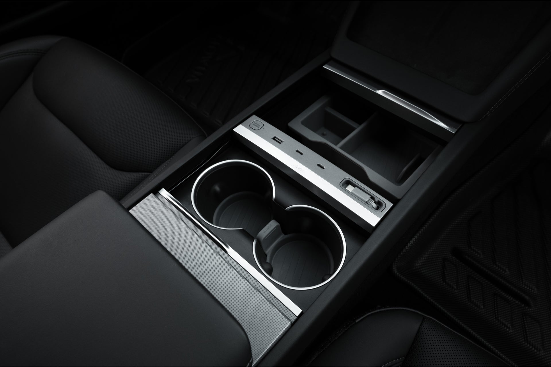 A close-up of the JOWUA 130W LED Hub for Tesla Model Y Juniper 2025+ / Model 3 2024+, featuring two cup holders, covered storage, and an electronic control interface with buttons and a dial. The sleek interior has a modern dark finish, seamlessly integrating charging and storage solutions.