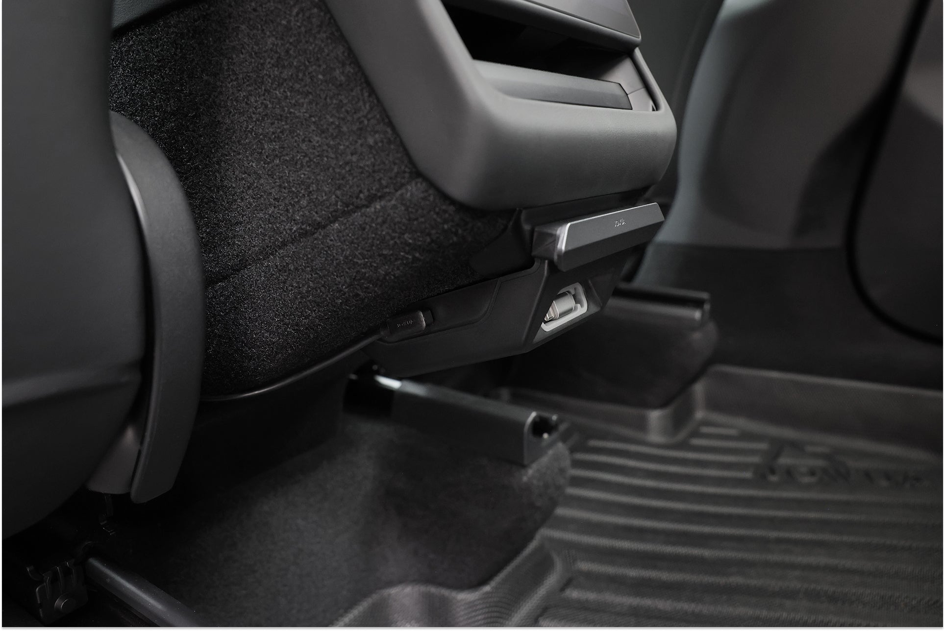 Close-up of the JOWUA 130W LED Rear Vent Hub (Model 3 Highland 2024+/Model Y Juniper 2025+), illuminating grooved floor mats and seat rails, with a storage pocket and custom-fit lighting for a clean, stylish rear car interior.